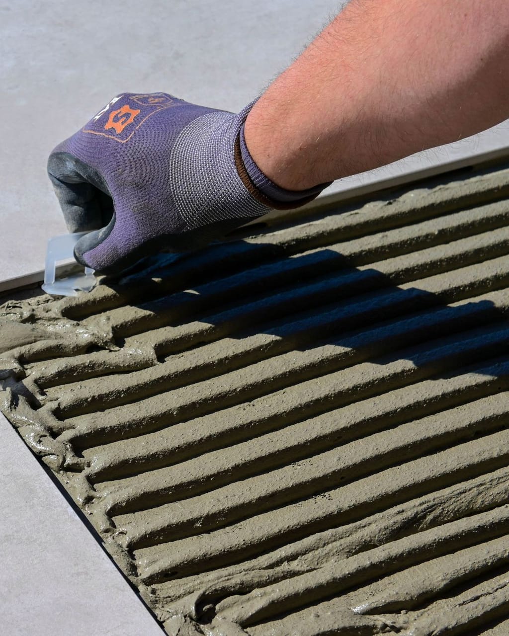 Behandschuhte Hand setzt Nivellierkeile in frischem Kleberbett.