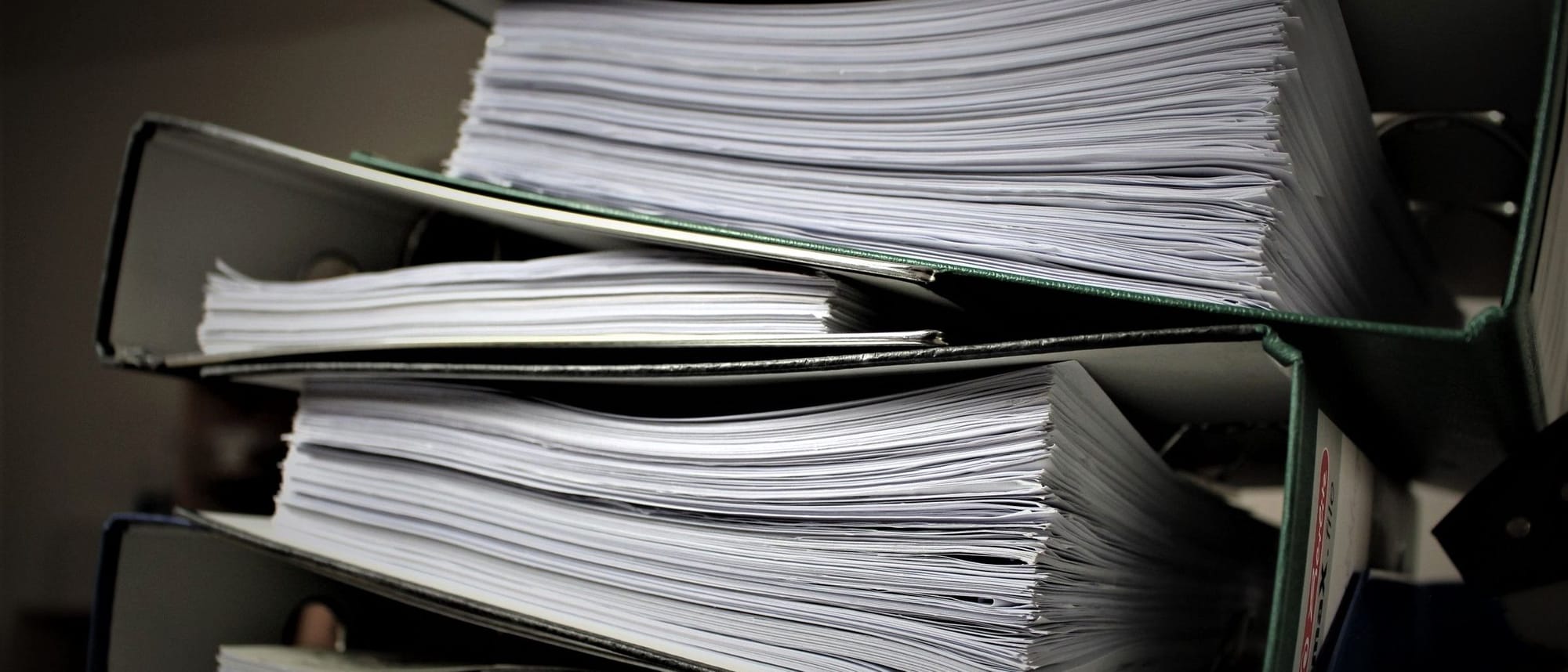 Gestapelte, prall mit Papier gefüllte Aktenordner.