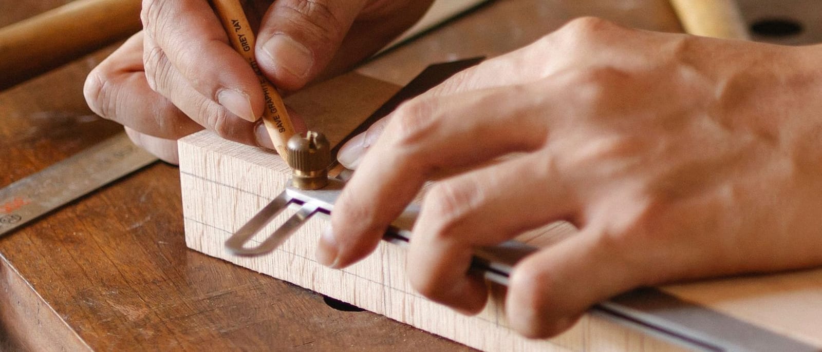 Hände reißen mit Streichmaß und Bleistift ein Werkstück auf der Hobelbank an.